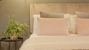 A neatly made bed with a beige headboard, multiple pillows, and a small potted plant on a side table.