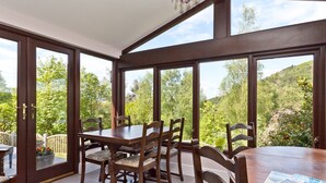Un espace repas avec une grande table et des chaises, de grandes fenêtres donnant sur un paysage verdoyant.