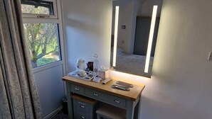 Una habitación pequeña y ordenada con un escritorio de madera, un espejo y una ventana con cortinas.