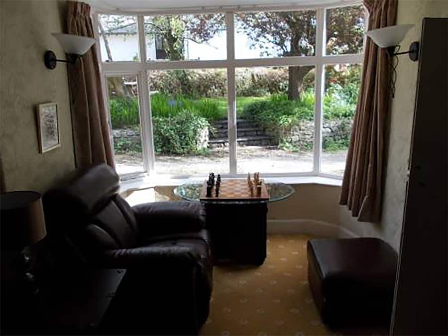 A room with a black leather sofa, a small round table with a chess set, and a large window with curtains.