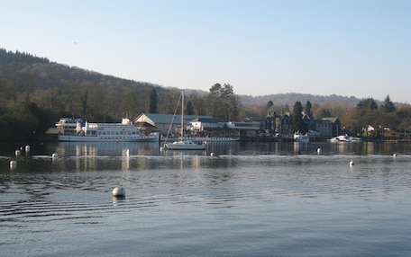 A waterfront area with boats, a building with a large window, and a forested hill in the background.