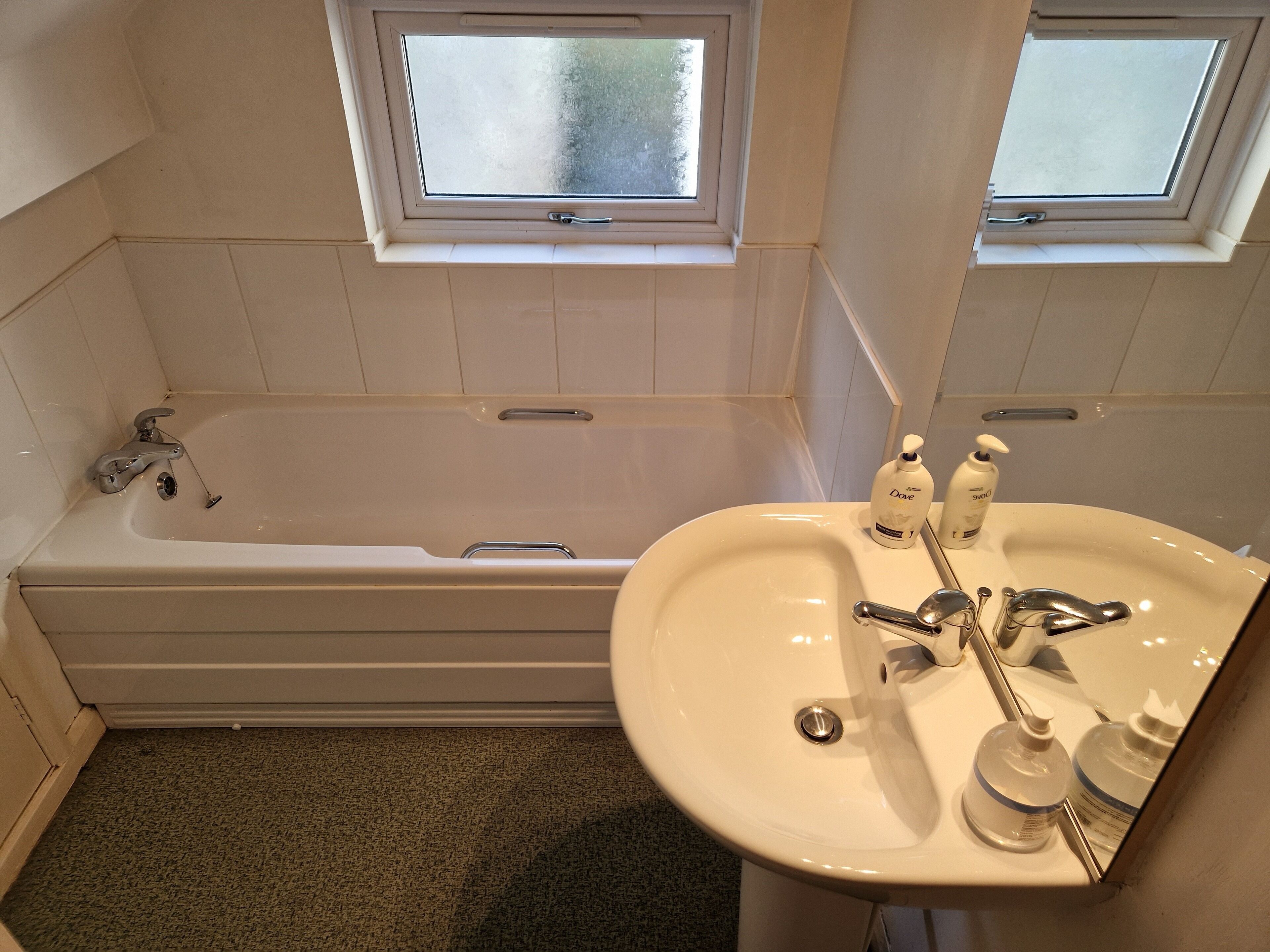 A bathroom with a bathtub, a sink, and two windows.