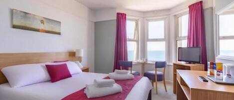 A hotel room with a bed, a desk, a television, and a window with curtains.