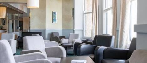 A hotel lobby with seating areas, a reception desk, and large windows with curtains.