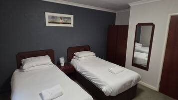 Ett hotellrum med två separata sängar, ett litet nattduksbord med en lampa, en inramad tavla på väggen och en spegel på dörren.