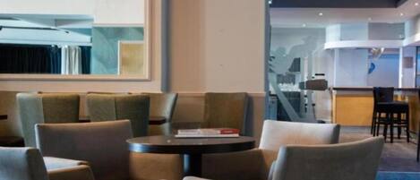 Un moderno vestíbulo de hotel con zona de estar que incluye sofás y una mesa redonda, un espejo grande y vistas al interior del hotel.