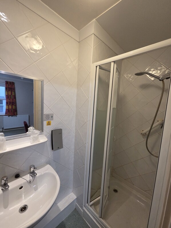Ein modernes Badezimmer mit einer Duschkabine, einem weißen Waschbecken und einem Spiegel darüber.
