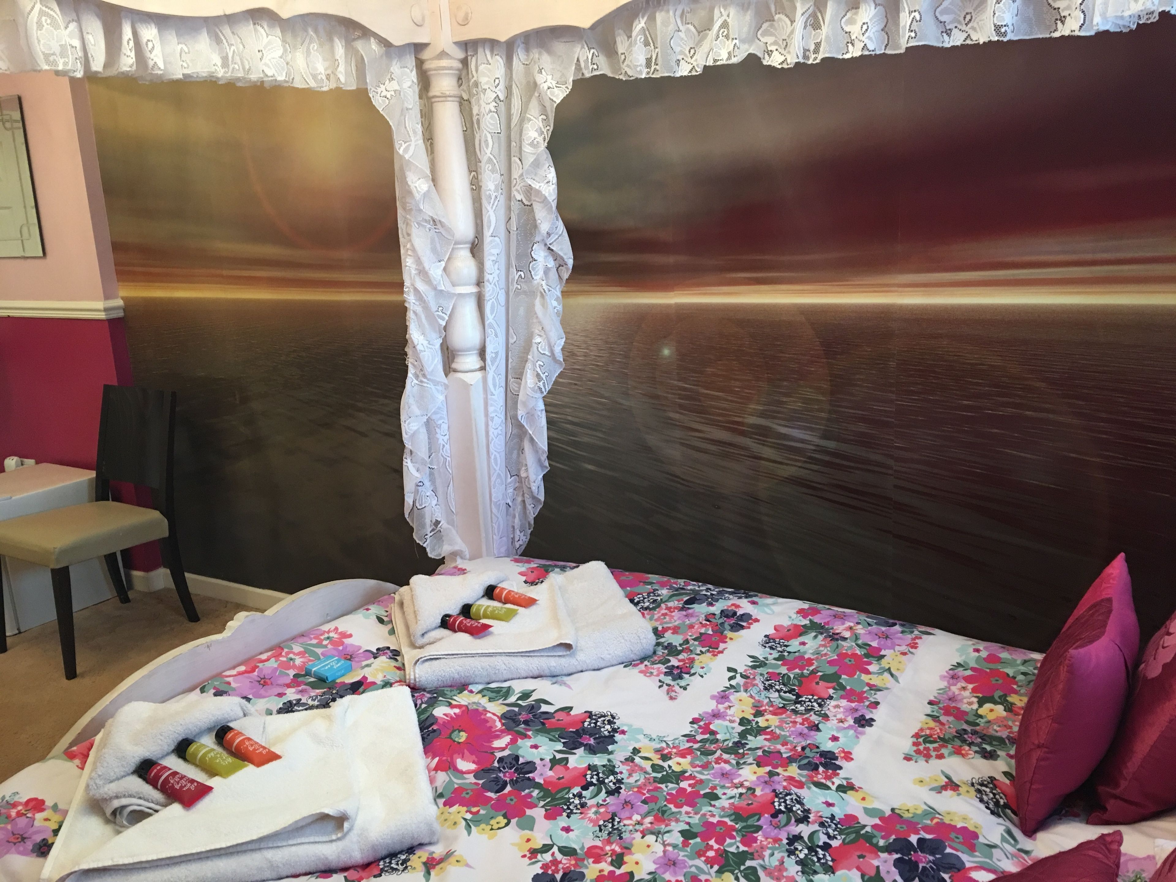 Una habitación de hotel con una colcha de flores, una cortina blanca y un cabecero de madera.