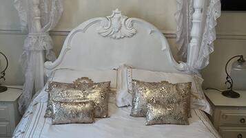 A four-poster canopy bed with ornate carvings, two decorative pillows, and a sequin-covered bedspread.