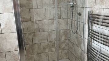 Una ducha con cerramiento de vidrio, un cabezal de ducha manual y un perchero adherido a la pared.