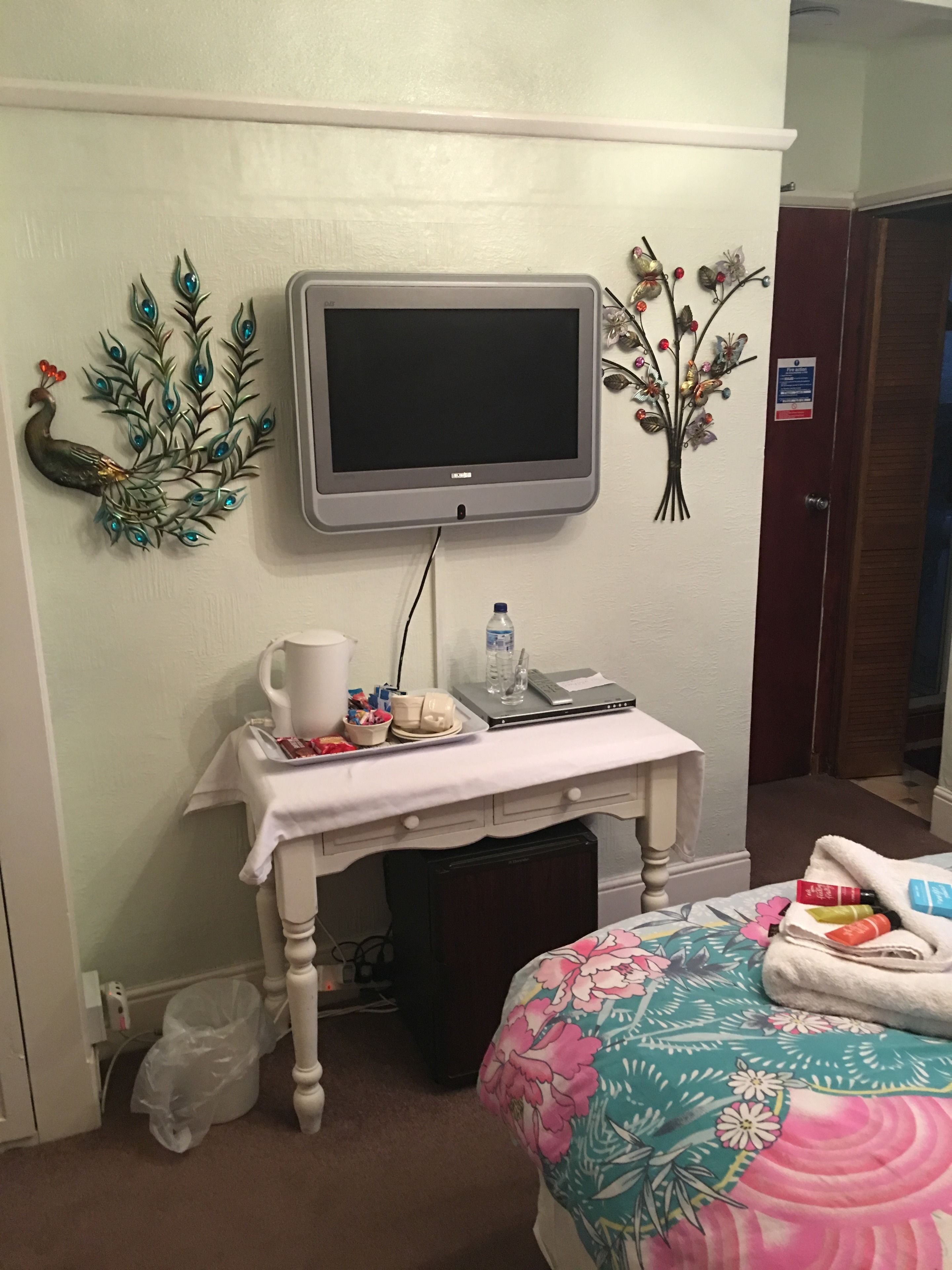 Une chambre d’hôtel équipée d’un lit, d’un bureau avec un ordinateur portable, d’une télévision et d’œuvres d’art décoratives au mur.