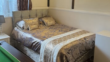 A bedroom with a bed, a nightstand, a lamp, a wall-mounted light, and a pool table.