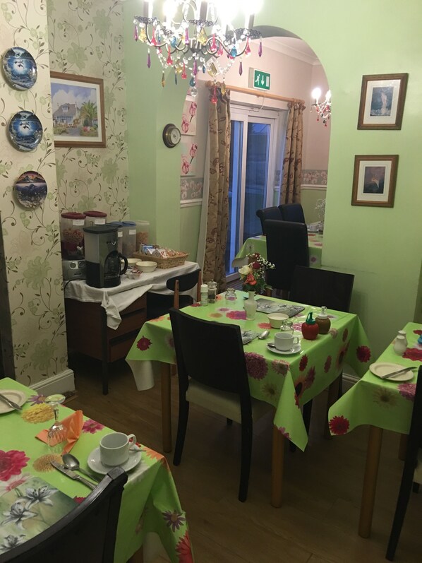 Un comedor con mesas cubiertas con manteles florales, sillas y diversos utensilios de comedor.