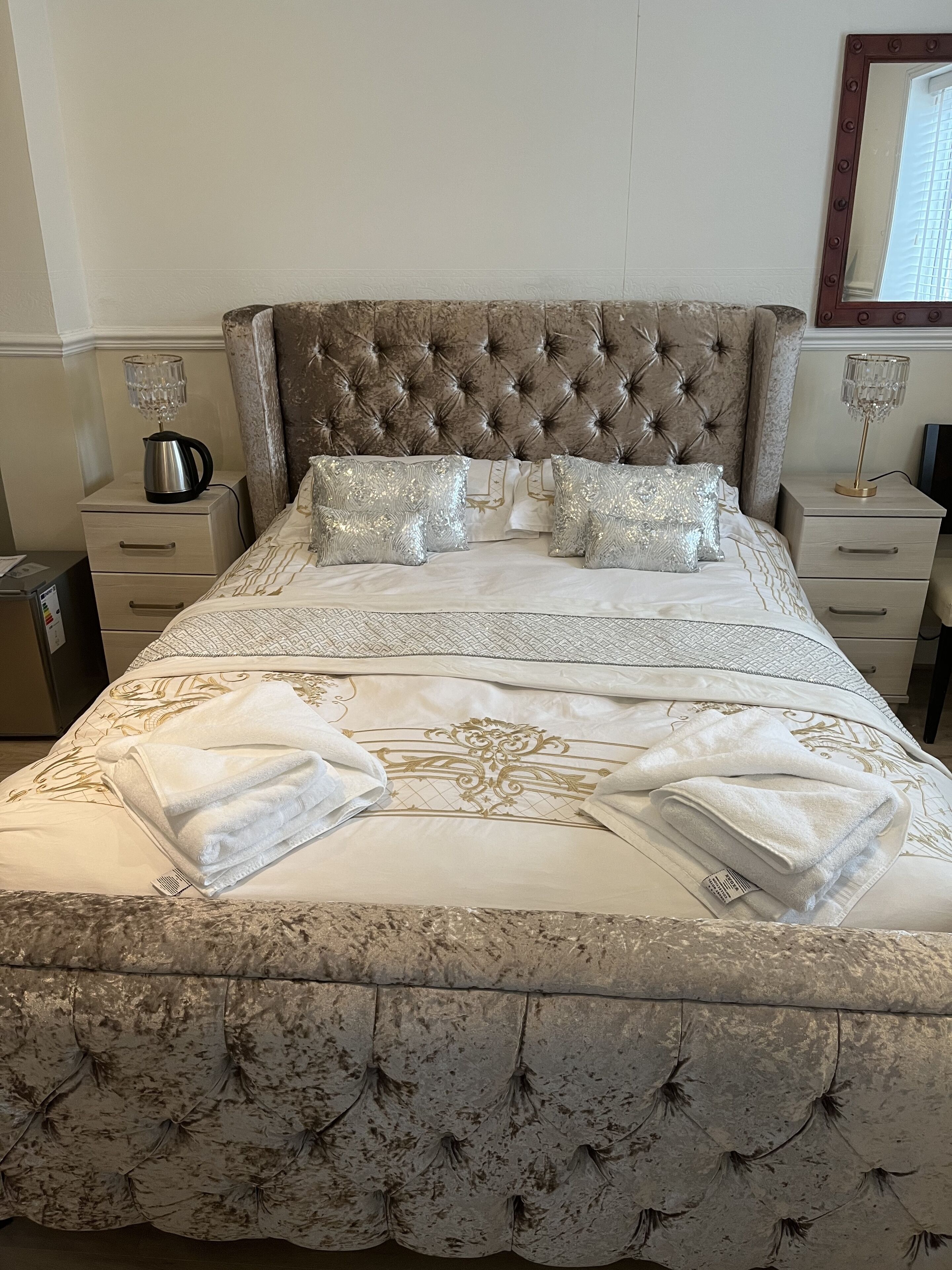 A neatly made bed with a tufted headboard, decorative pillows, and folded towels.
