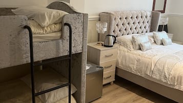 Un dormitorio con una cama individual, una cama matrimonial con cabecera capitonada, una mesita de noche con lámpara y un armario pequeño.