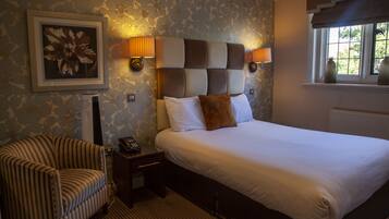 A hotel room with a bed, a chair, a nightstand, and a framed picture on the wall.