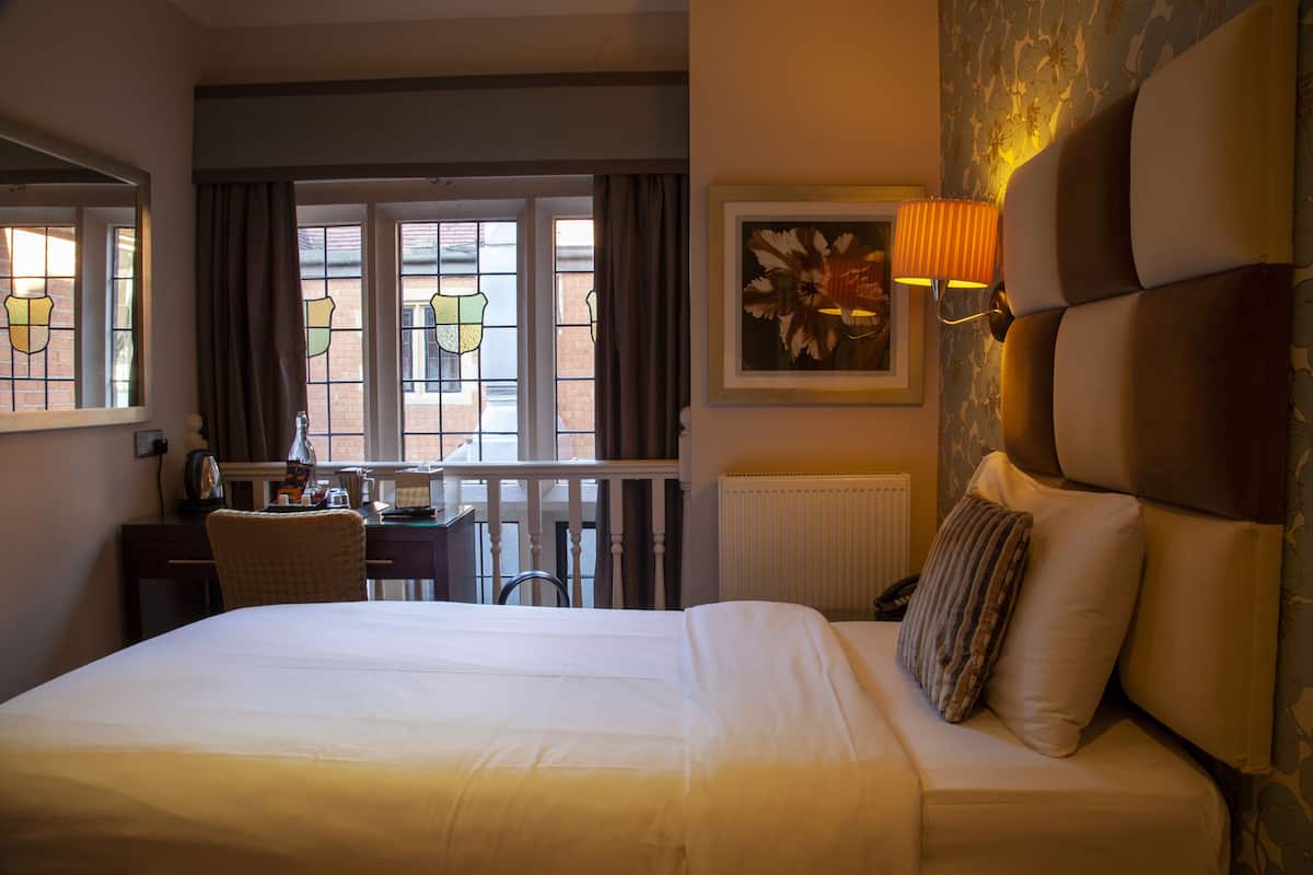 Une chambre d’hôtel avec un grand lit, un bureau, une chaise et une fenêtre avec des rideaux.