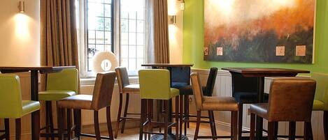 Une pièce comprenant un coin bar avec plusieurs tabourets et une table, une grande peinture abstraite au mur et une fenêtre avec des rideaux.
