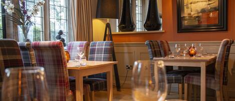 A dining area with plaid upholstered chairs, a wooden table, and wine glasses.