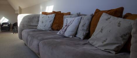 Un canapé gris agrémenté de plusieurs coussins, un petit fauteuil et un tapis à motifs dans une pièce dont le plafond est incliné et qui offre une vue sur le ciel.
