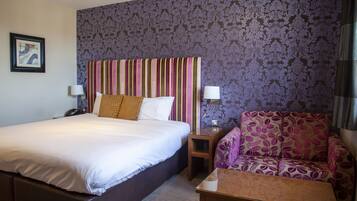 Ein Hotelzimmer mit einem großen Bett, einem Schlafsofa, einem Nachttisch und einer Wand mit ornamentalem Wandpapier.
