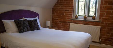 A bedroom with a large bed, a brick wall, a window with a view, and a radiator.