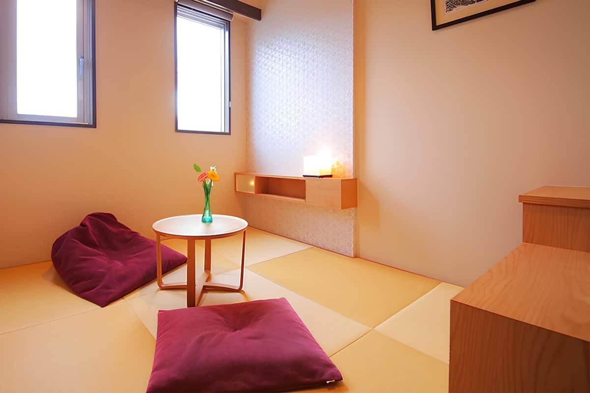 Een knus kamertje met tatami vloer, een lage tafel met een bloevas en een houten kast.