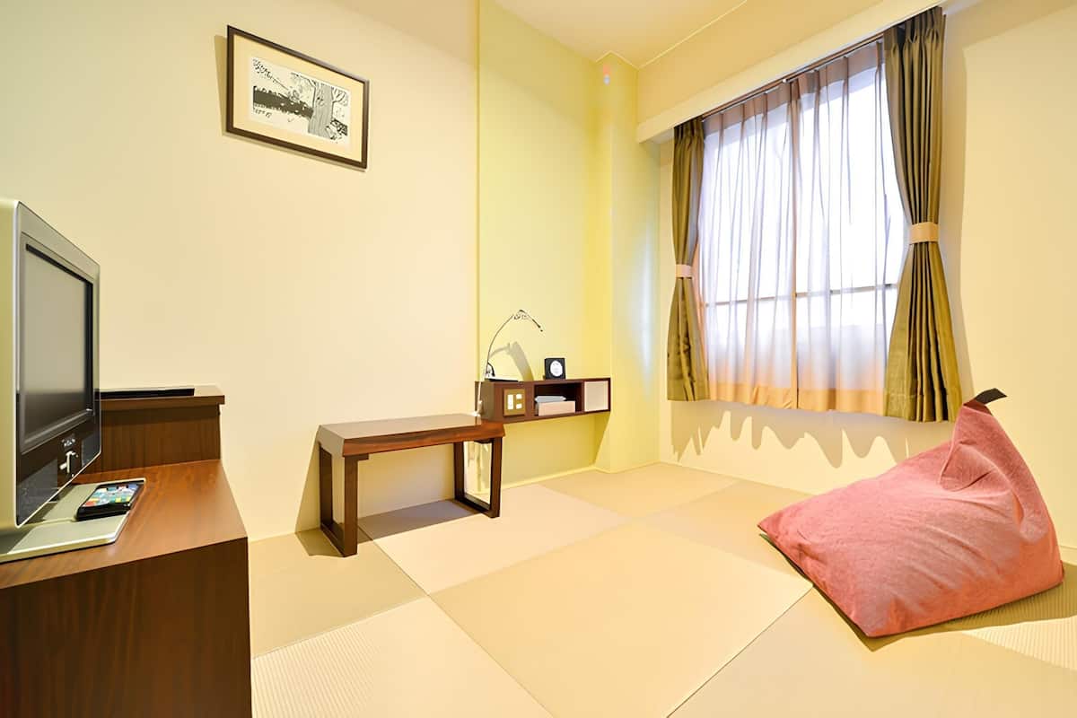 Een kamer met een televisie, bureau, stoel, bed en een raam met gordijnen.