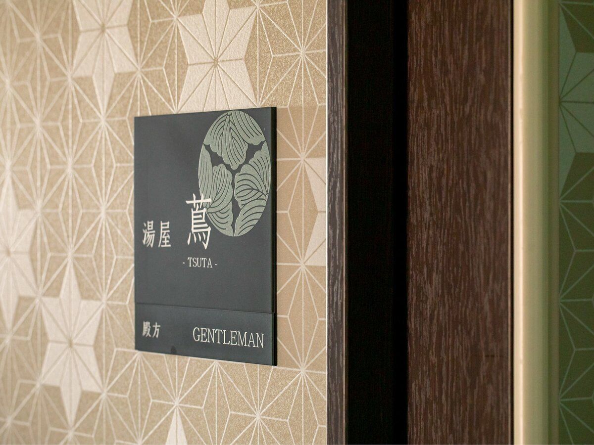 A hotel room with a geometric patterned wallpaper and a sign indicating a 'Gentleman' room.