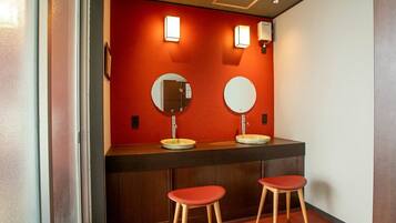 A restroom with two sinks, each with a mirror and a light above. There are two stools in front of the sinks.