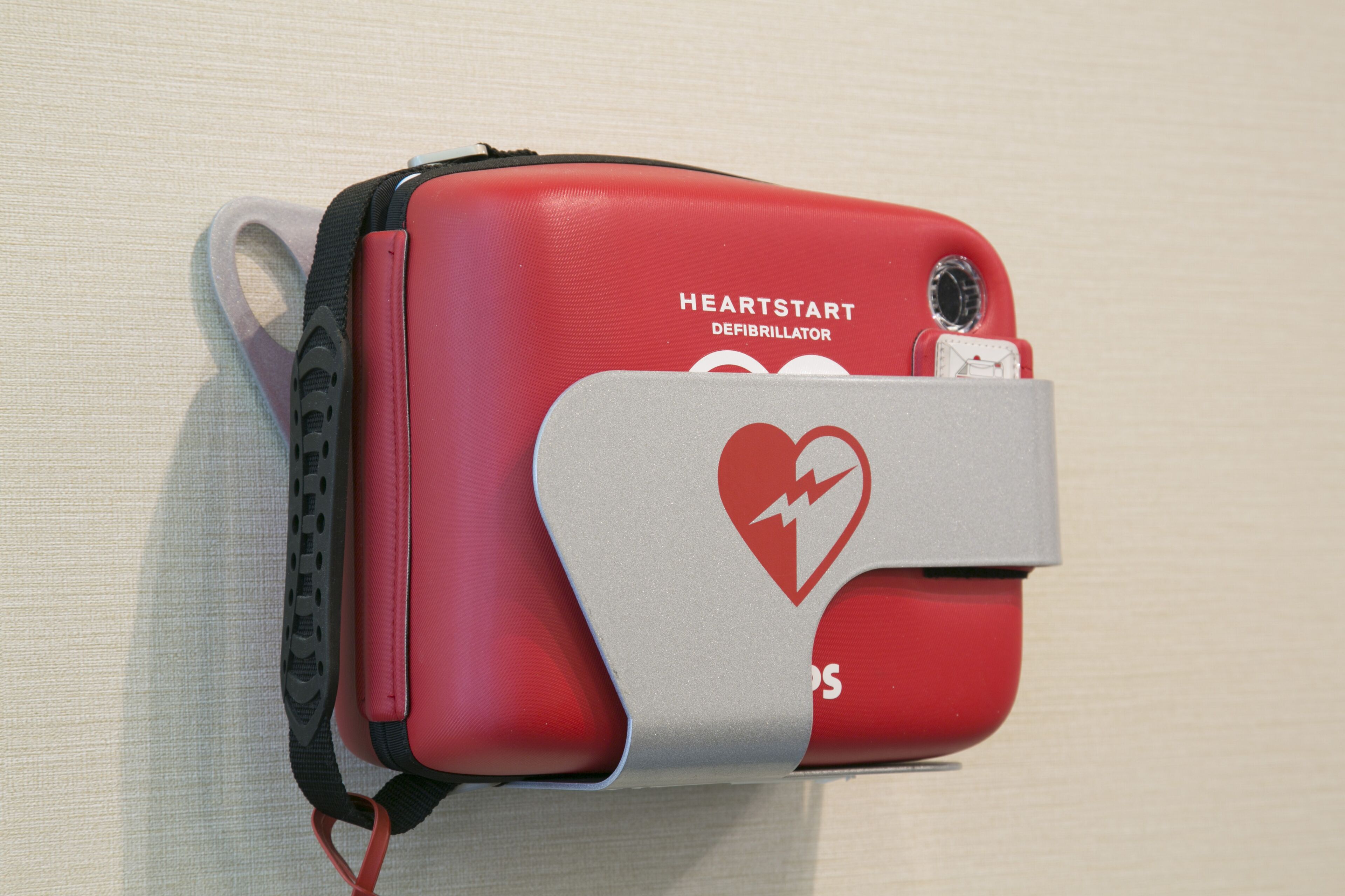 Een rode defibrillator met een hartsymbool en de tekst 'HEARTSTART DEFIBRILLATOR'.