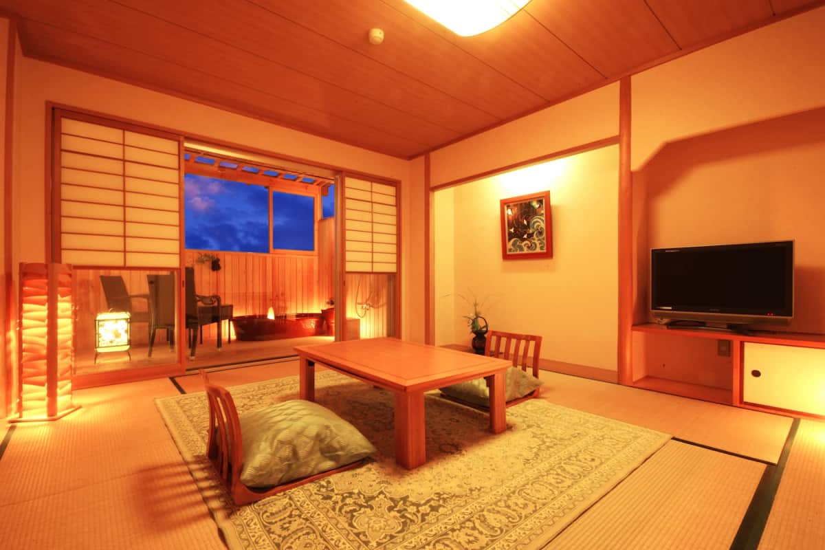 A traditional Japanese room with tatami flooring, a low wooden table, a television, and sliding doors leading to another room.