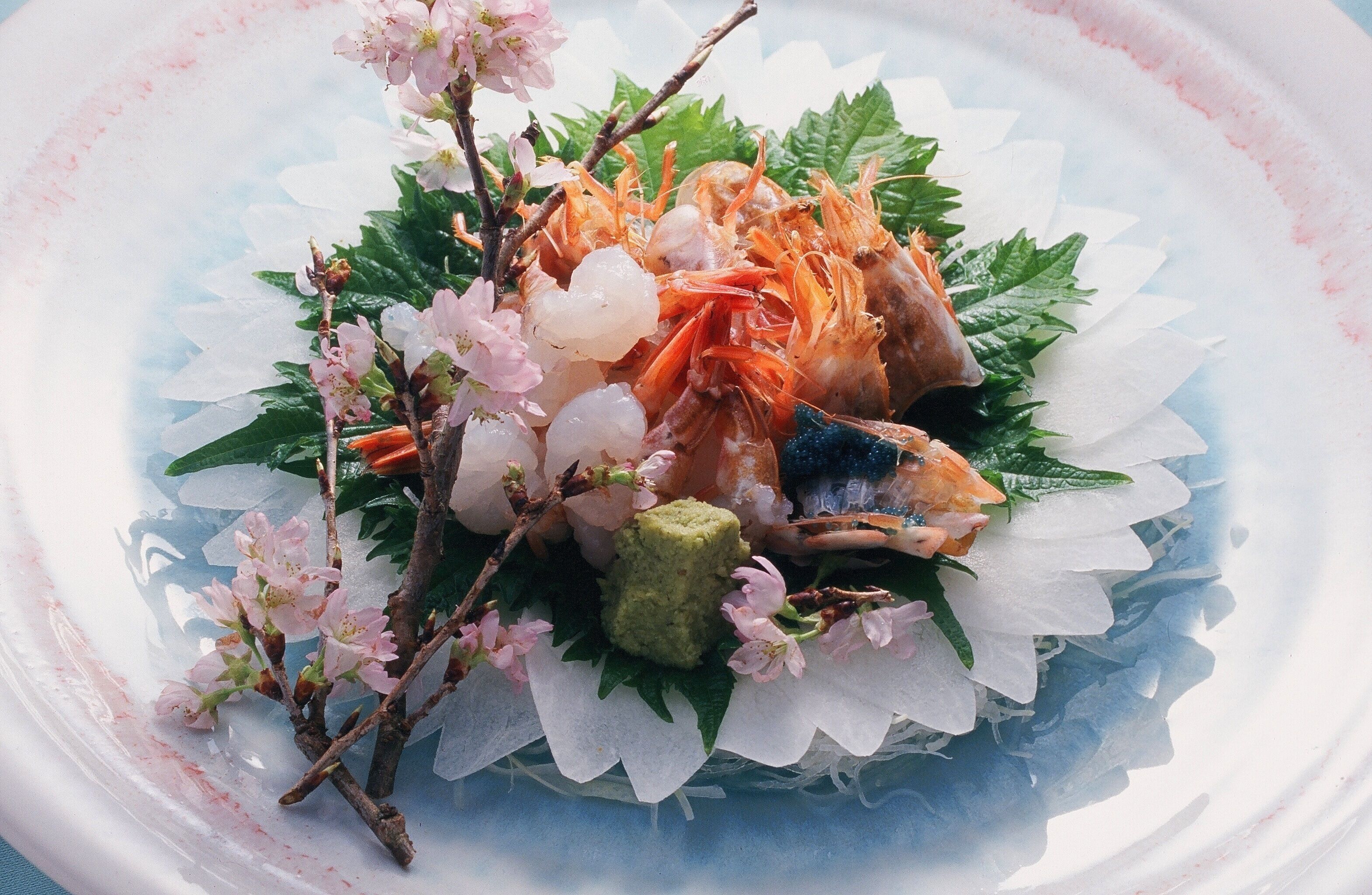 A seafood dish with shrimp, scallops, and a green garnish on a plate with a floral design.