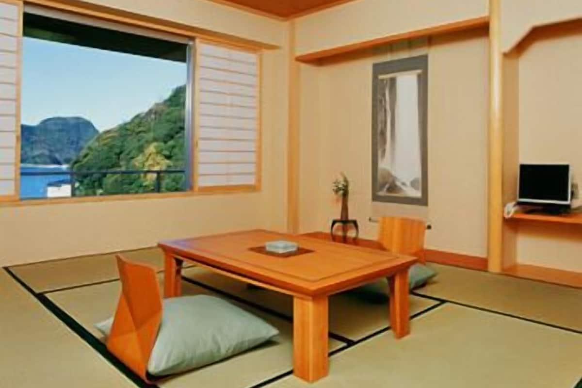 A traditional Japanese room with tatami flooring, a low table, and a view of a mountainous landscape through a large window.
