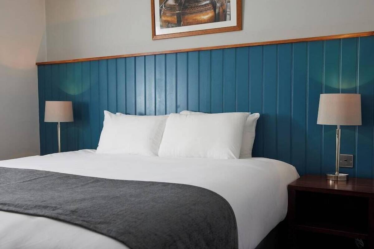 Une chambre d’hôtel avec un grand lit, deux tables de chevet, une tête de lit bleue et un tableau encadré au mur.