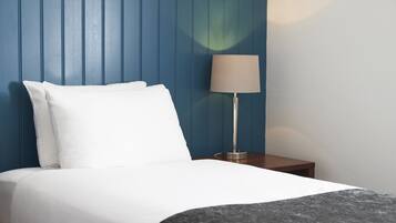 A neatly made bed with white bedding, a wooden headboard, and a bedside table with a lamp.