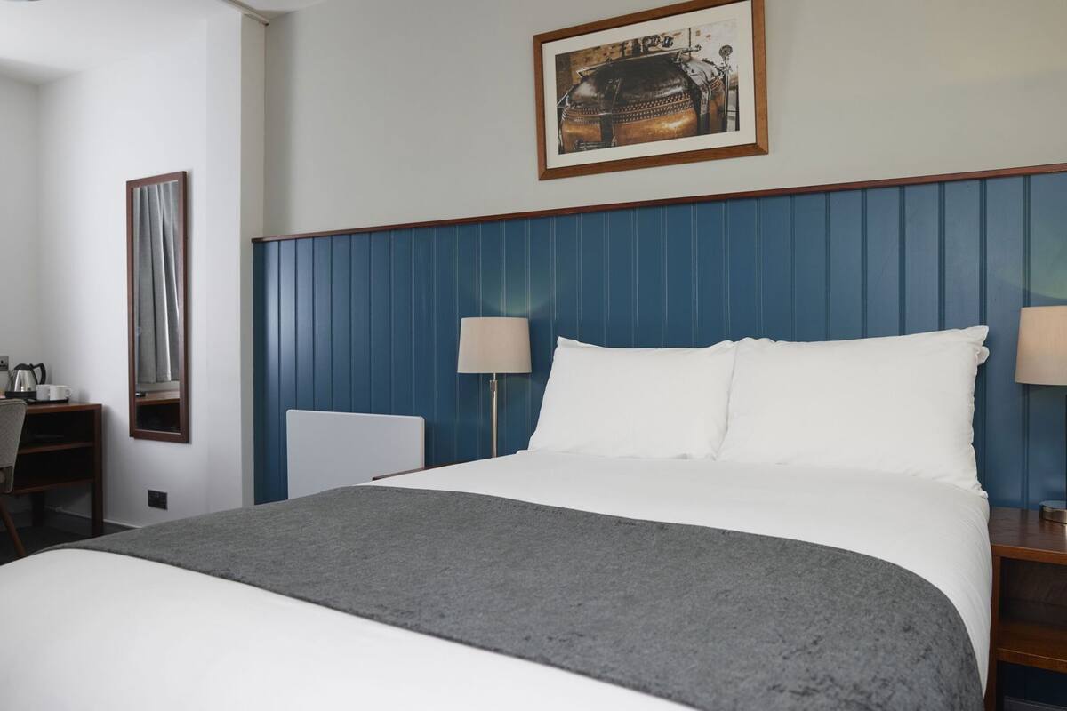 Une chambre d’hôtel avec un grand lit, deux lampes de chevet, un bureau avec une chaise et un tableau encadré au mur.