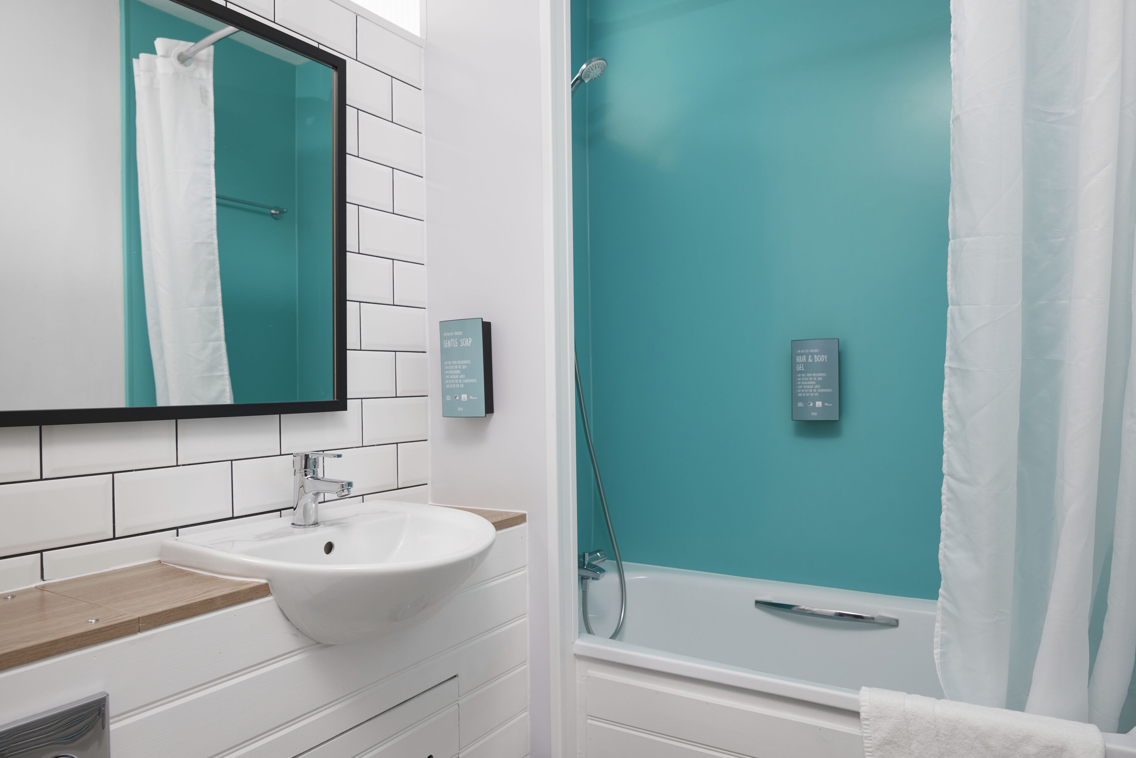 A modern bathroom with a white sink, a glass-enclosed shower, and a teal accent wall.