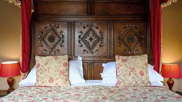 Una cama con ropa de cama floral, un cabecero de madera con paneles decorativos y cortinas rojas.