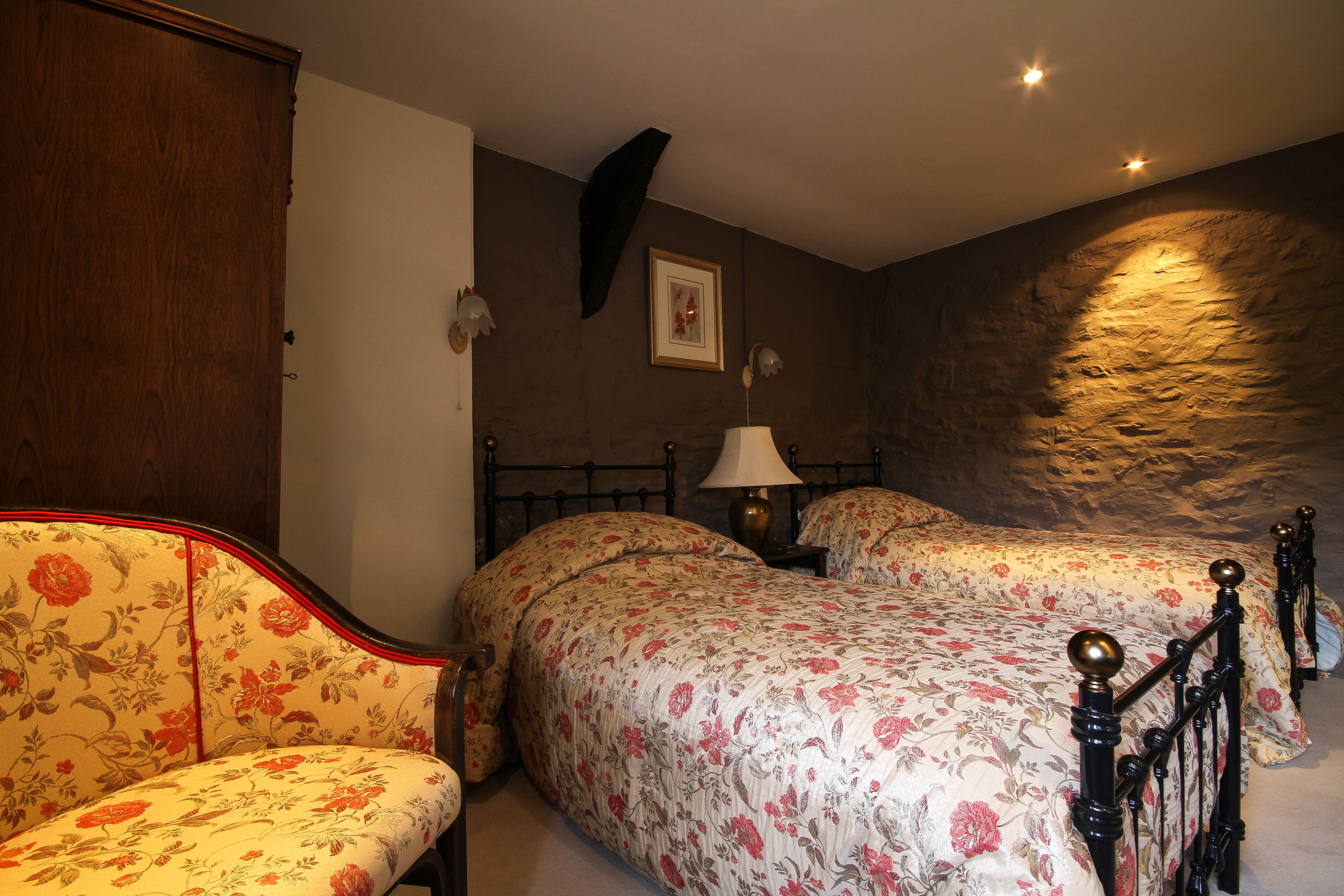Un dormitorio con dos camas, un armario de madera, una mesita de noche con una lámpara y un cuadro enmarcado en la pared.
