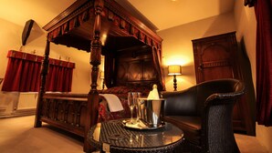 Una cama con dosel y cuatro columnas, un sillón de cuero, una mesita redonda con bandeja y una mesita de noche con lámpara.