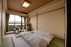 Quarto de hotel com cama, uma pequena mesa com cadeira, televisão e ar condicionado.