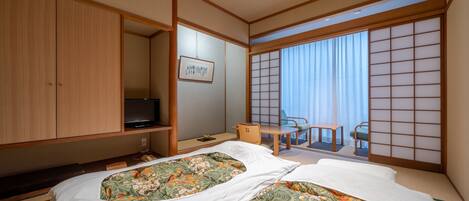 Habitación de hotel con dos camas, televisión, escritorio y un panel corredero estilo shoji.