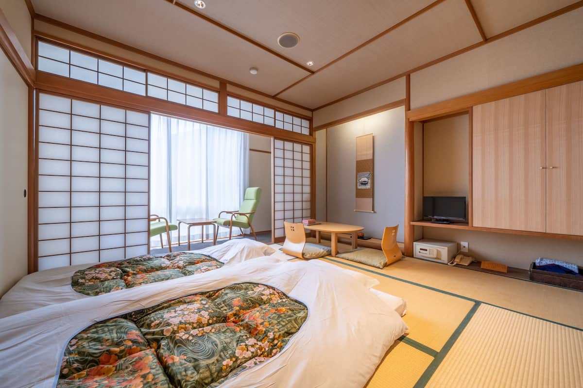 A traditional Japanese-style room with tatami flooring, a futon bed, a television, and a sliding door.