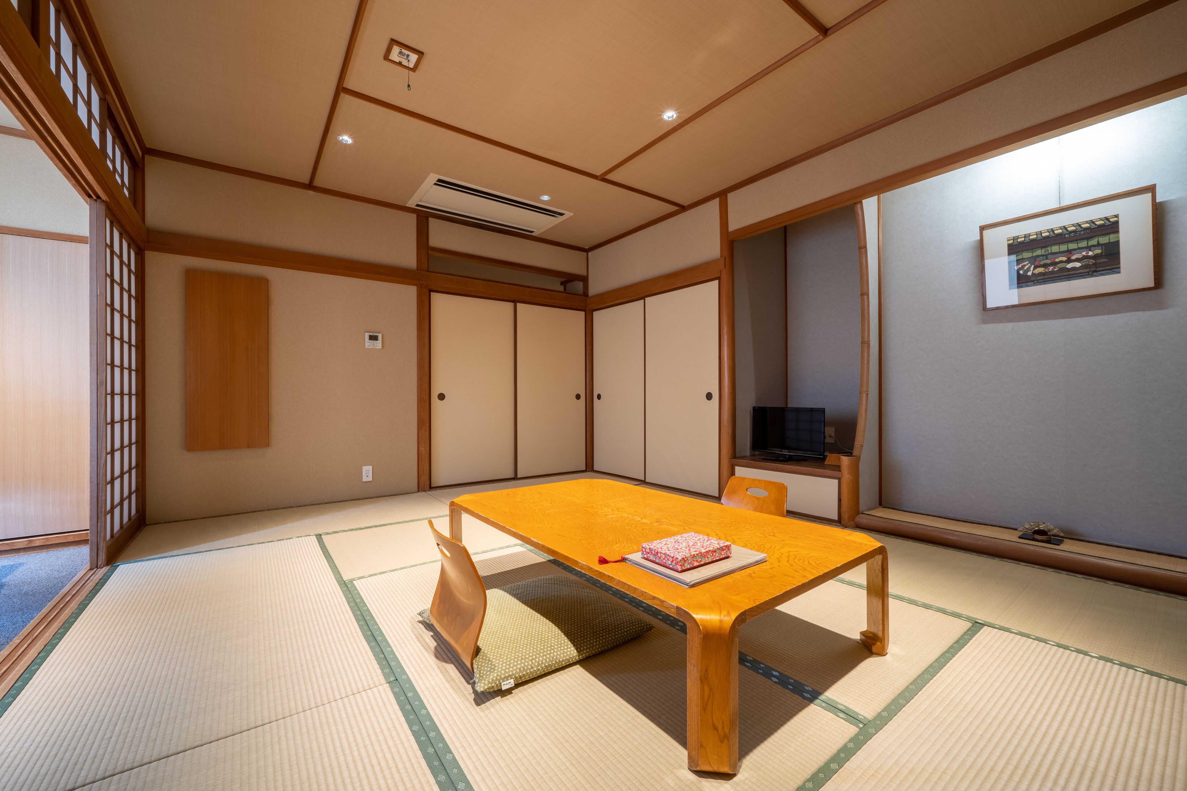A traditional Japanese room with tatami flooring, a wooden table, a cushion, sliding doors, and a framed picture on the wall.