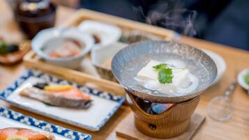 A hot pot setup with tofu and vegetables, surrounded by various dishes on a wooden table.