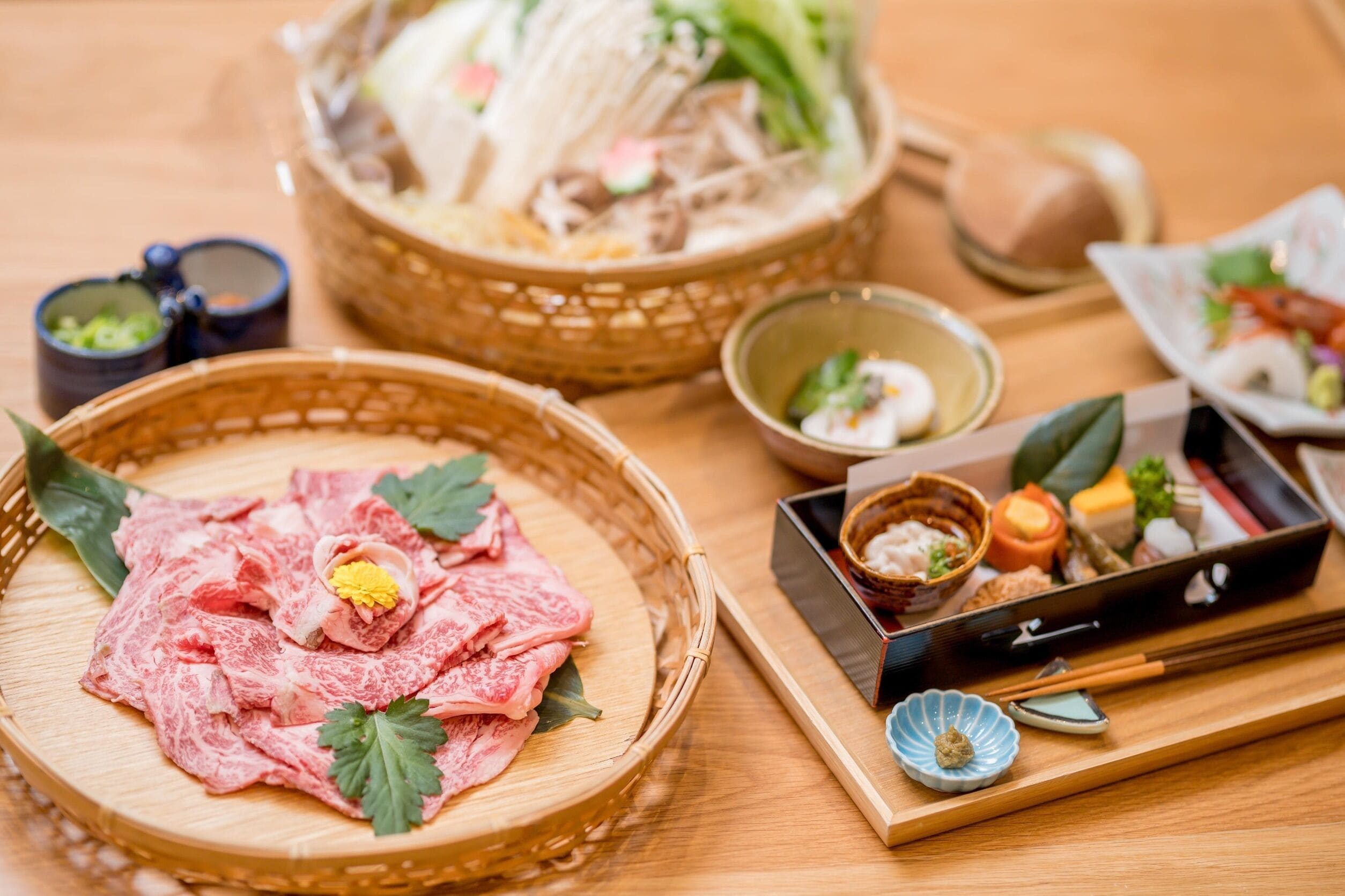 Puinen pöytä, jonka päällä on punottu kori, jossa on raakaa lihaa, pieni kulho kastiketta sekä tarjoilualusta, jossa on syömäpuikot ja lautanen.