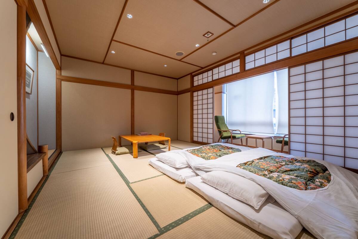 A traditional Japanese room with tatami flooring, a futon bed, a wooden table, and a sliding door.