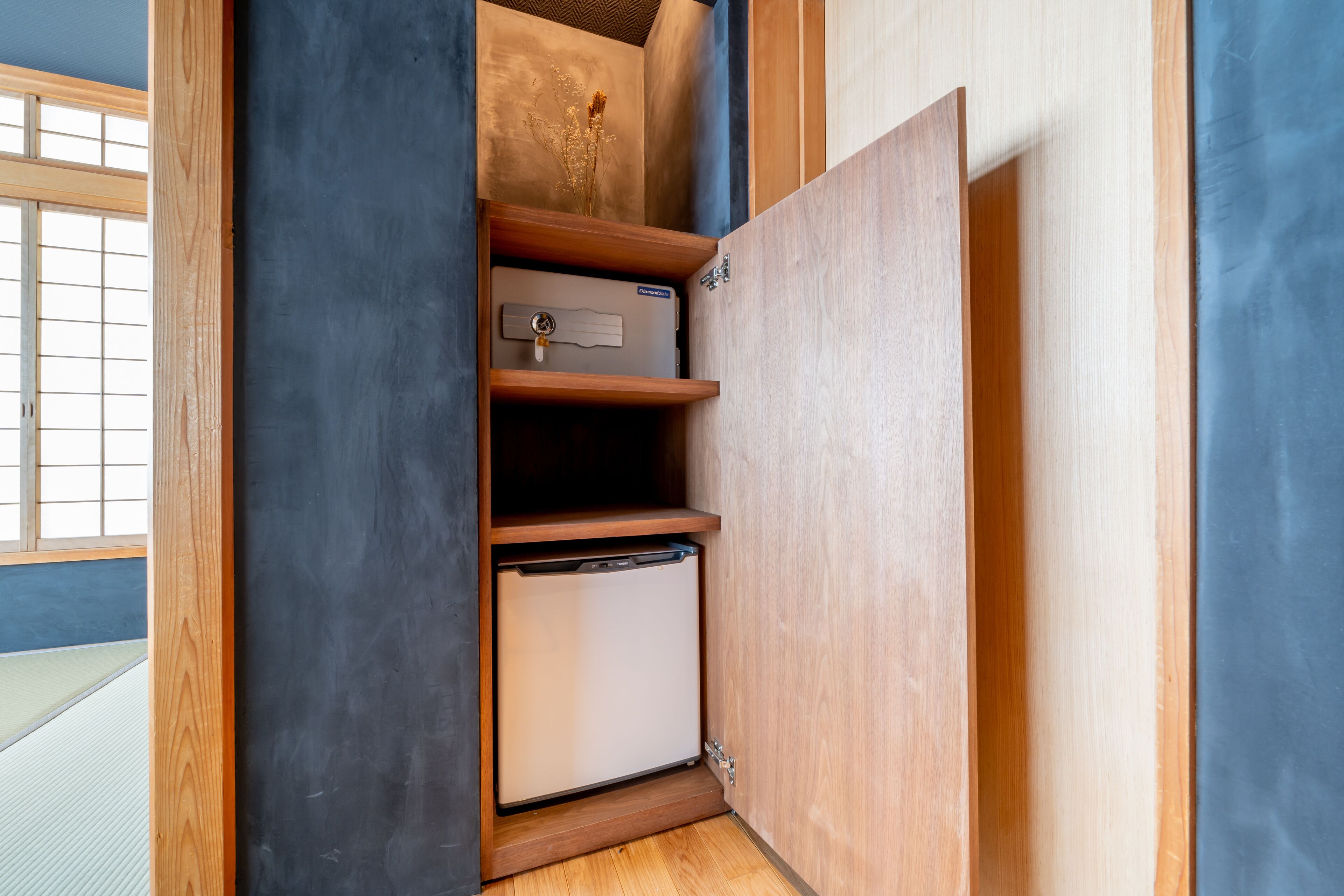 Un mueble compacto con refrigerador pequeño, un gabinete con llave y un estante con un objeto decorativo.