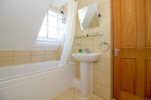Un baño con bañera, lavamanos, espejo y puerta de madera.